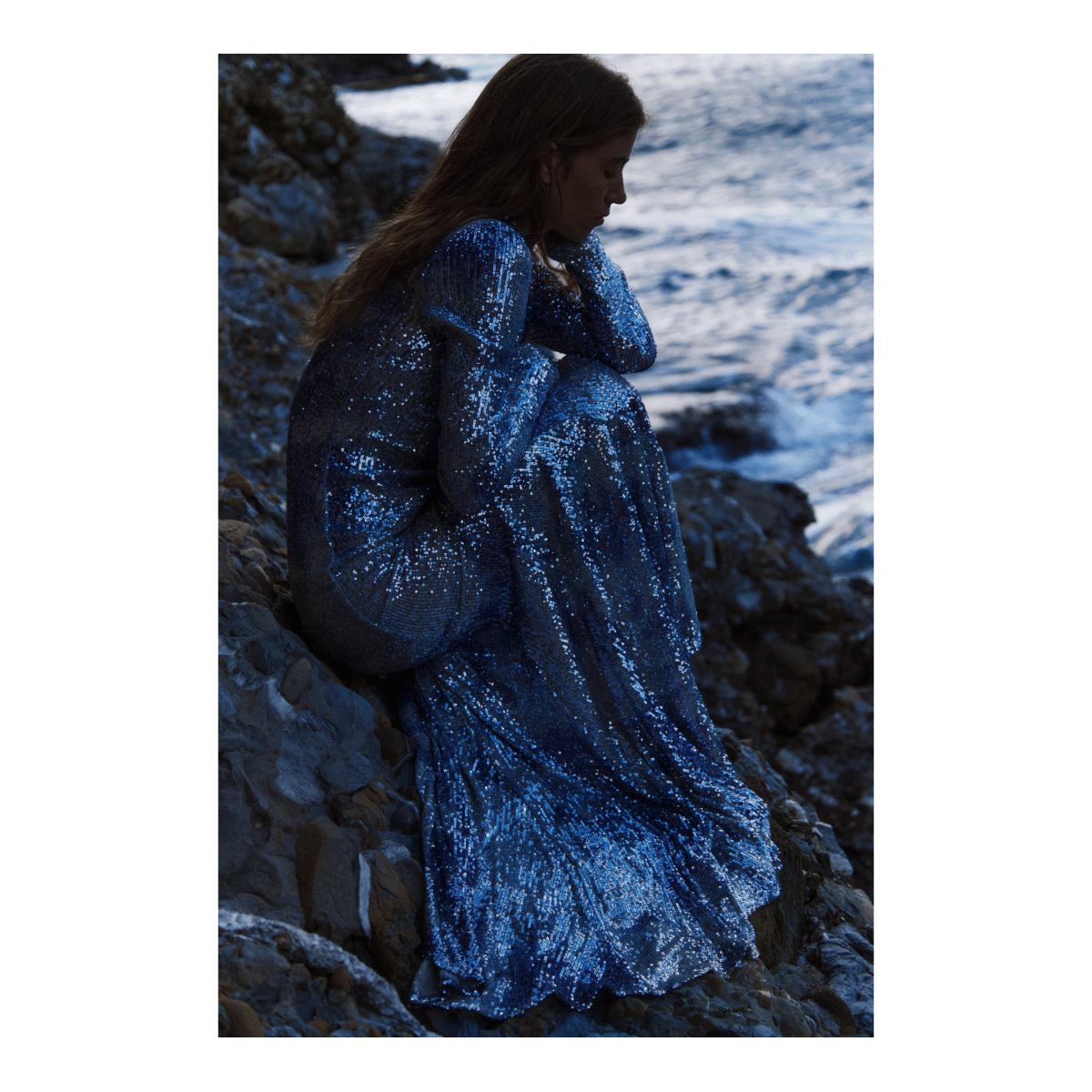 DELFINA, abito a sirena in paillettes mélange, indossato sugli scogli con il mare sullo sfondo.