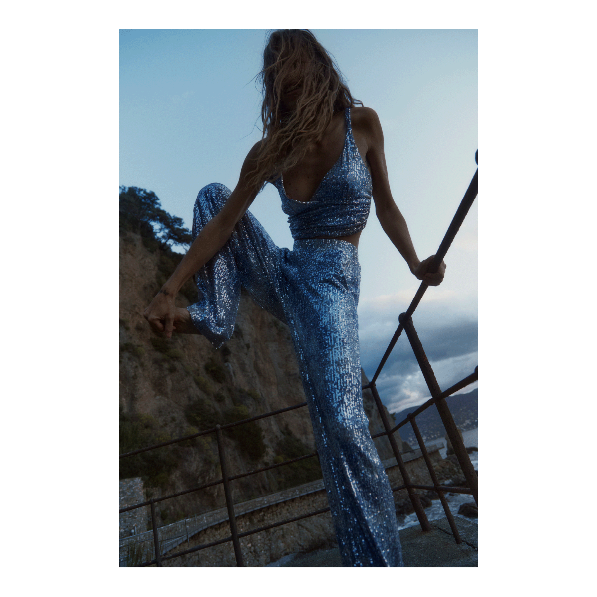 MAXIE, pantaloni palazzo in paillettes mélange, indossati in un completo coordinato sul mare.